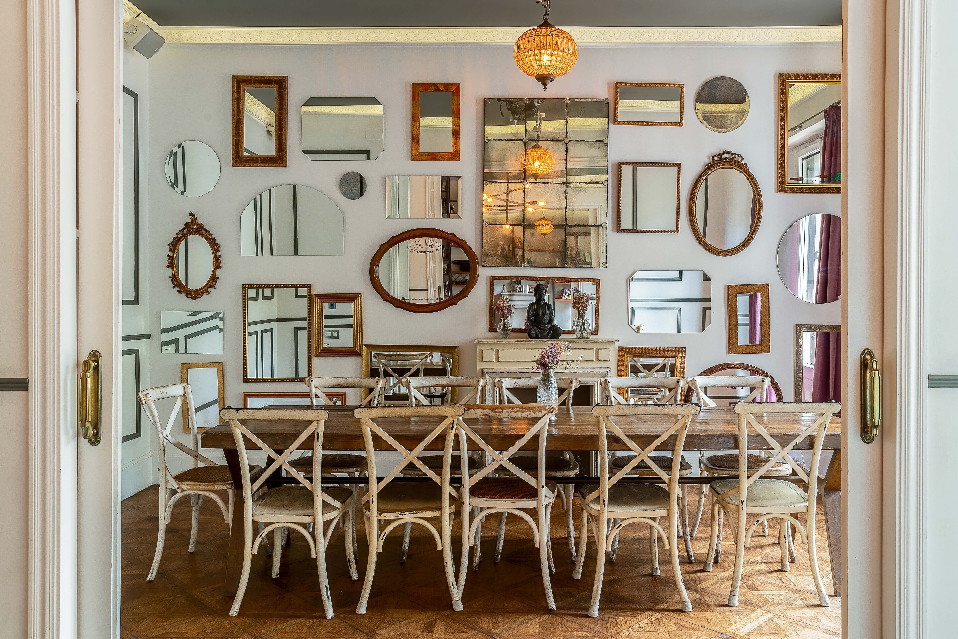 A dining area with a wooden table and chairs, surrounded by various mirrors on the walls.