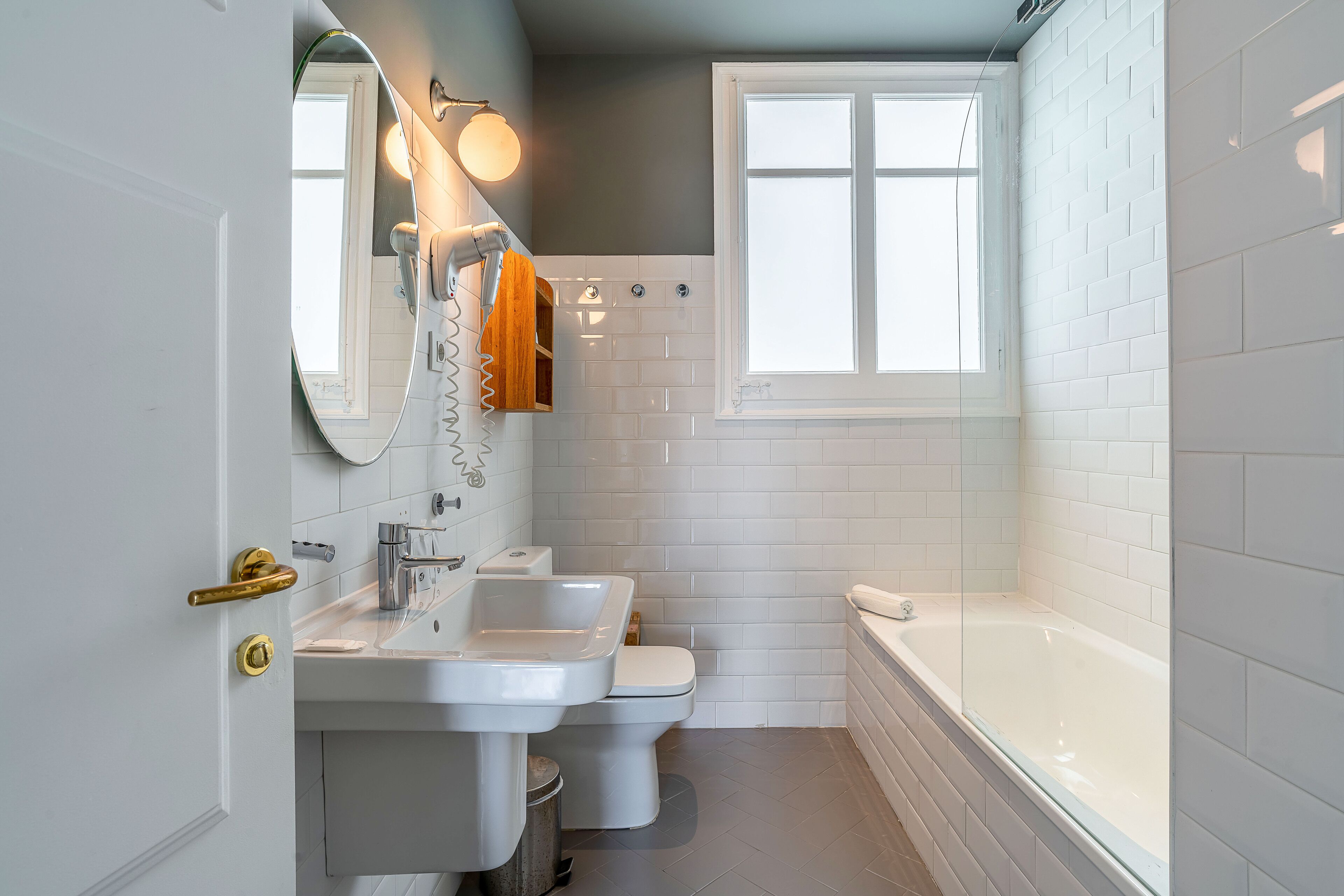 A bathroom with a sink, toilet, and bathtub, featuring white tiles and a window.