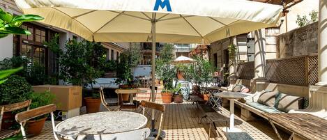 An outdoor patio with a round table, chairs, a bench, and an umbrella with a logo.