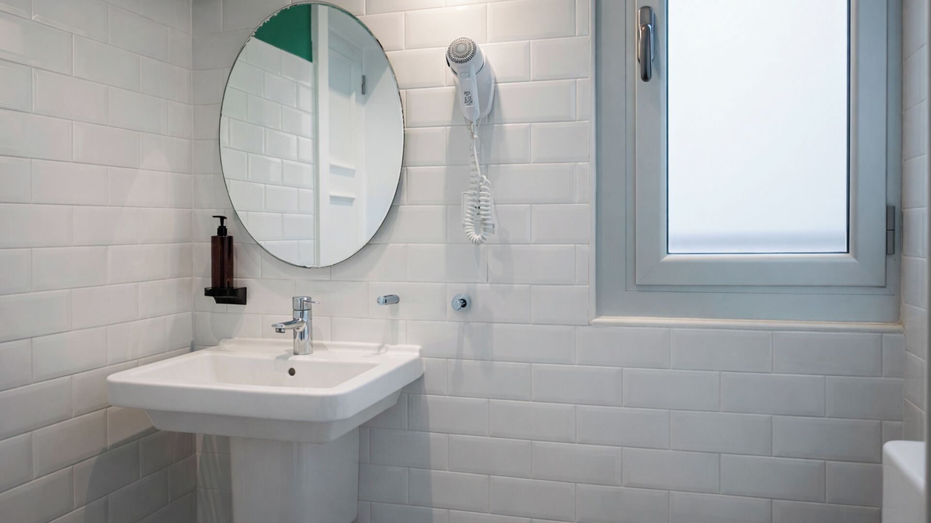 A bathroom with a white sink, a mirror, a hairdryer, and a window.