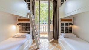 A dormitory room with bunk beds, a ladder, and a balcony with curtains.