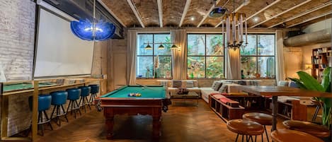 A cozy bar area with a pool table, bar stools, and a seating area with a sofa and chairs.