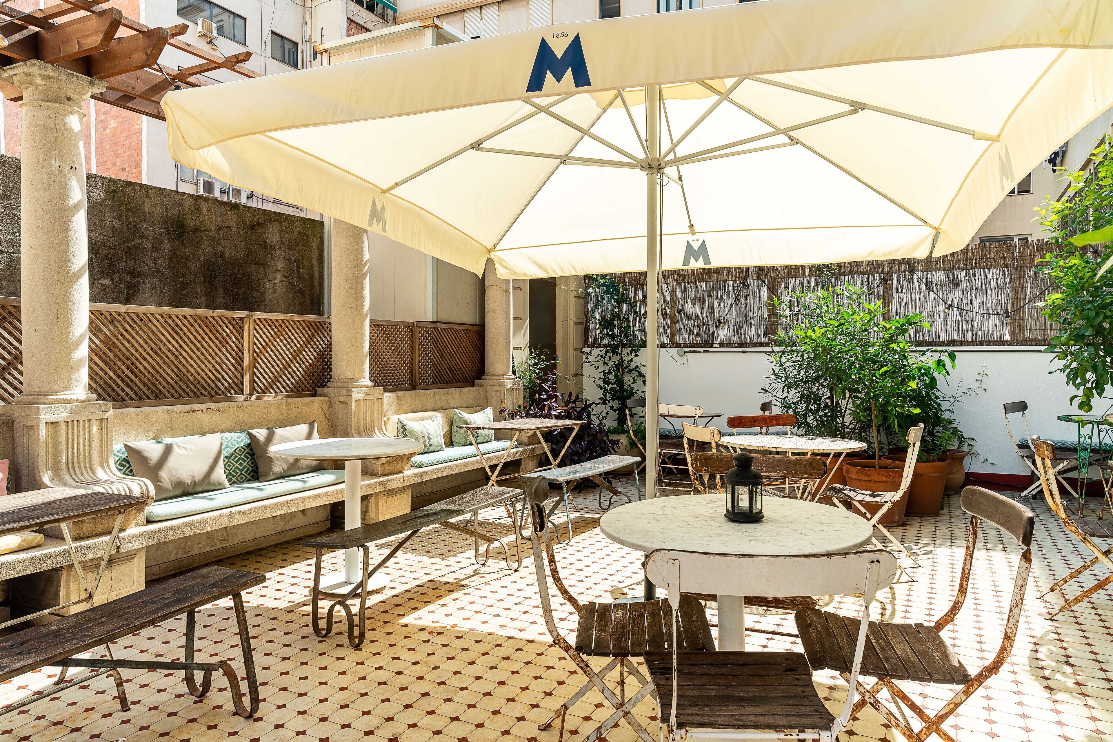 Eine Terrasse im Freien mit großem Sonnenschirm, Sitzgelegenheiten und Tischen.