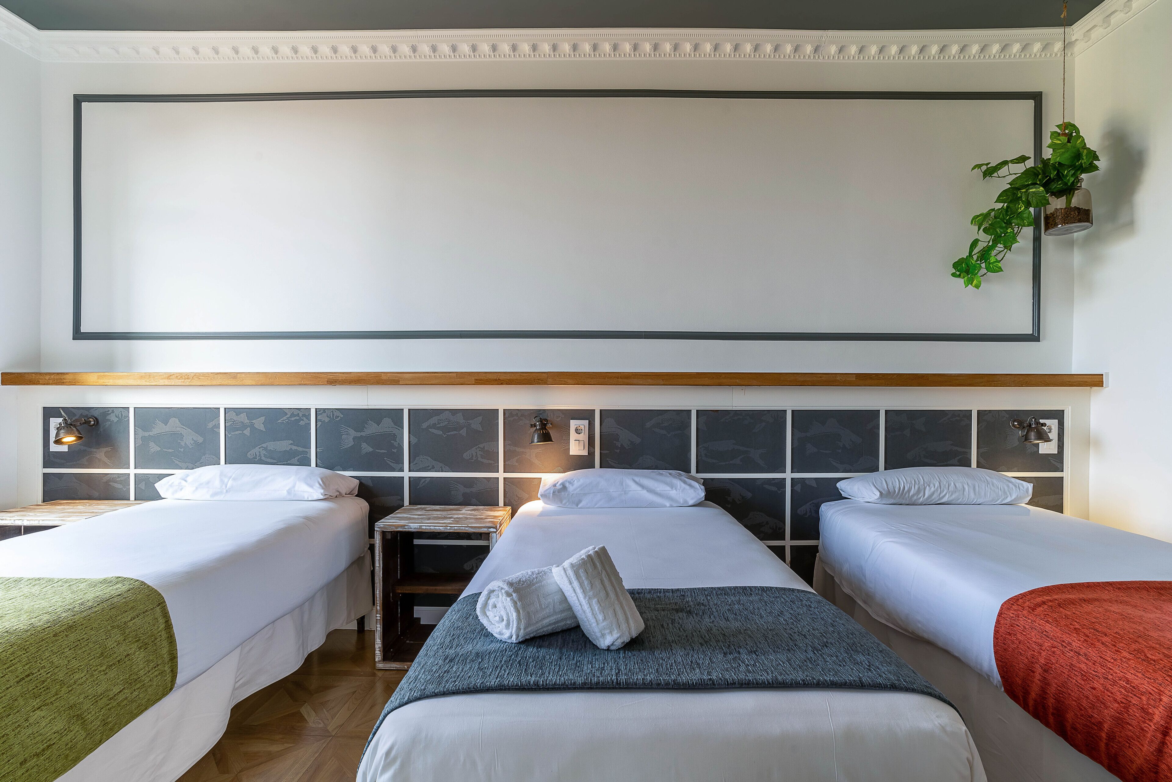 Habitación de hotel con dos camas individuales, un banco de madera, una mesita pequeña y una planta en la pared.