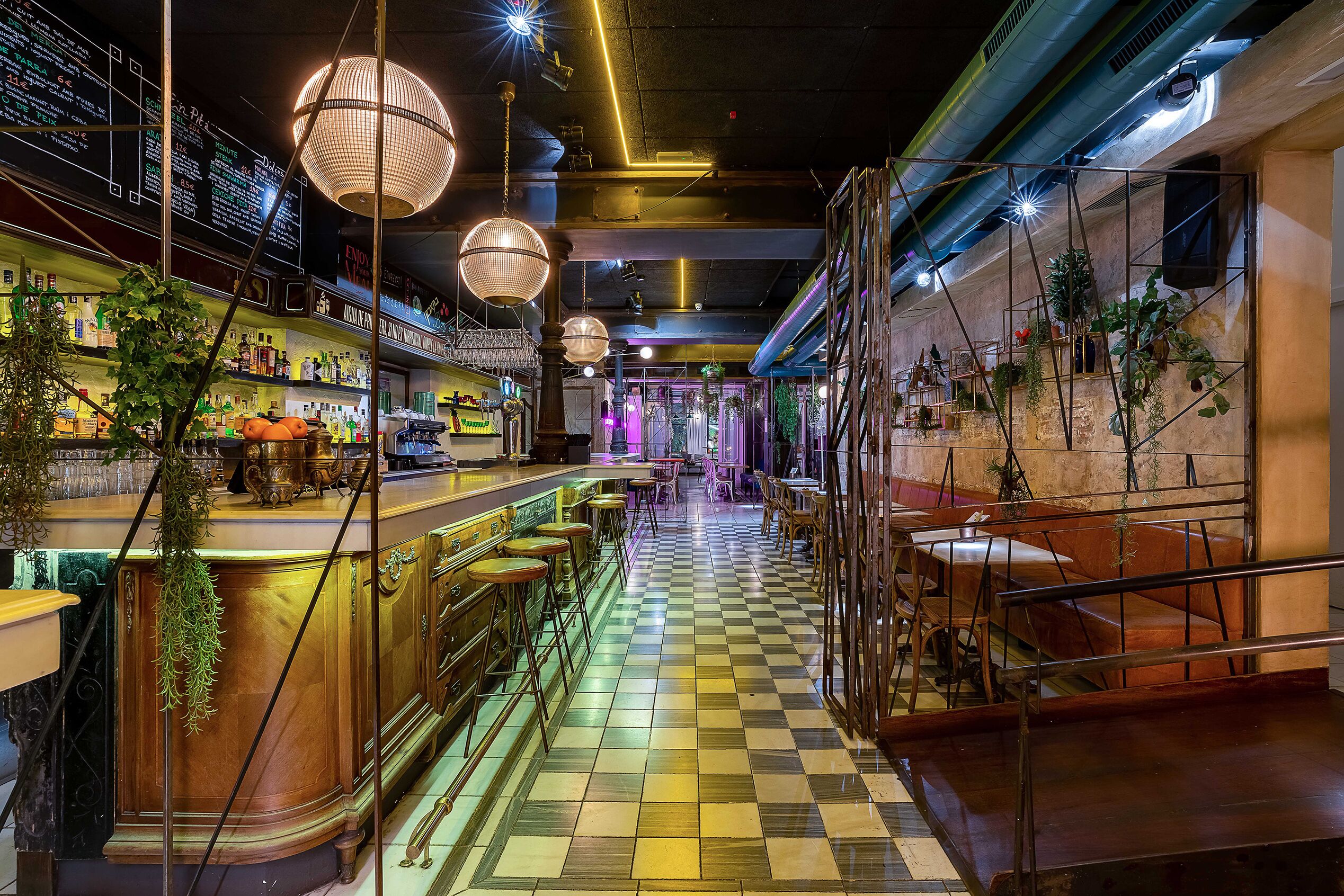 A bar area with checkered flooring, hanging lights, and bar stools.