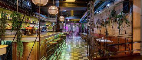 A bar area with checkered flooring, hanging lights, and bar stools.
