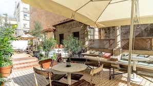An outdoor patio with a round table and chairs, surrounded by potted plants and a large umbrella.