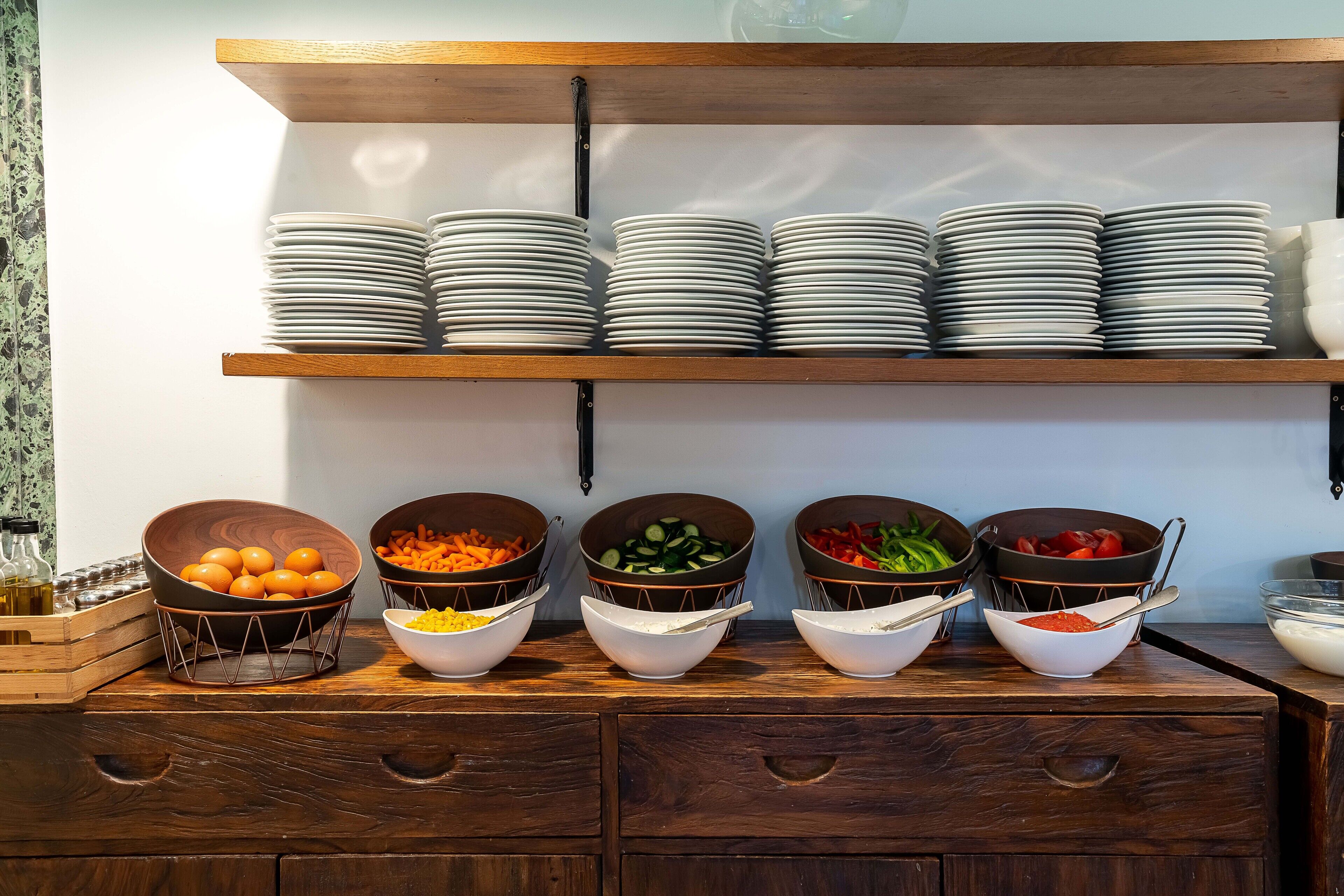 Montaje de bufé con varios recipientes de comida y platos apilados en estantes.
