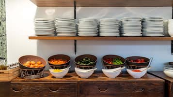 Montaje de bufé con varios recipientes de comida y platos apilados en estantes.