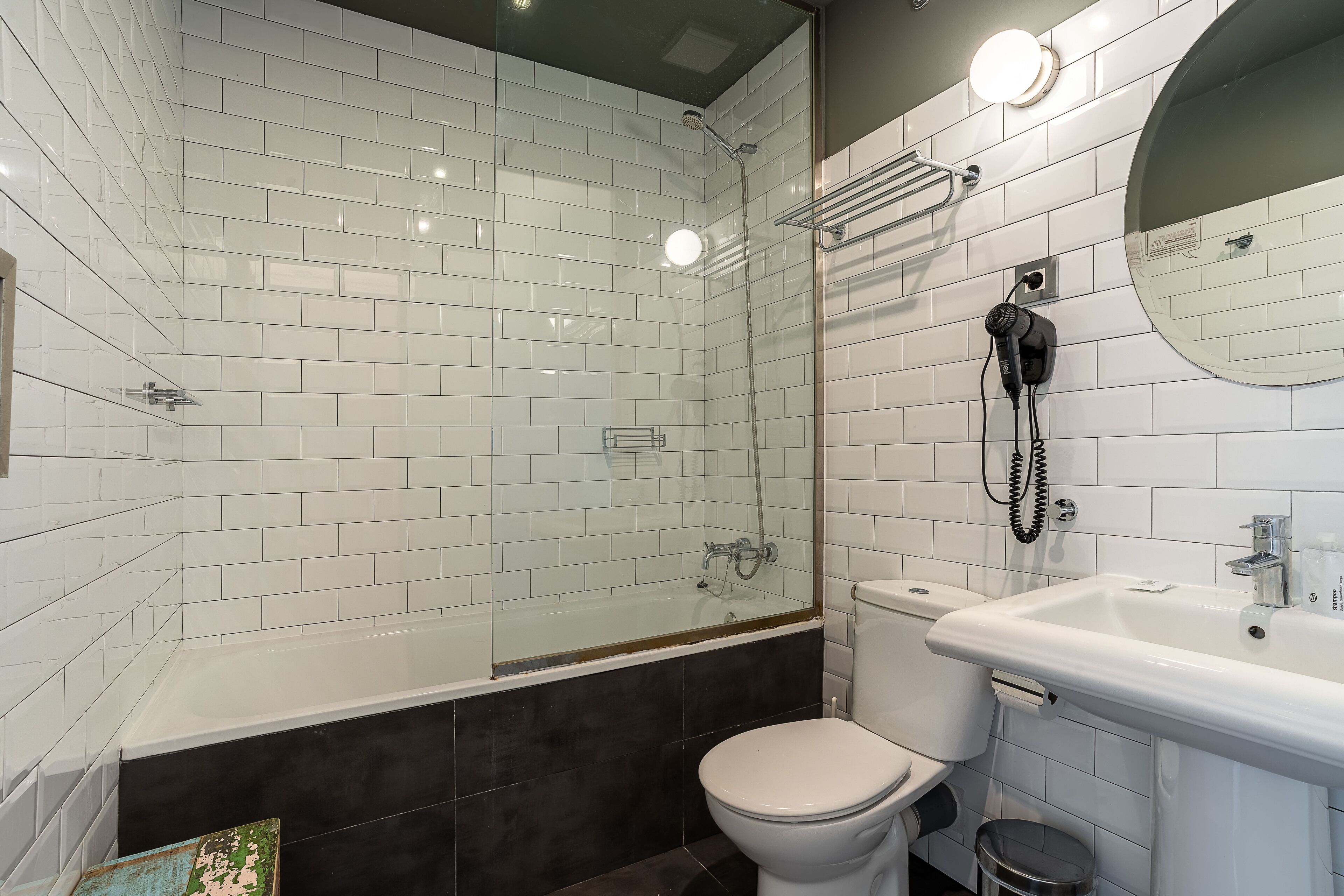 A modern bathroom with white tiled walls, a glass-enclosed shower, a white toilet, and a sink with a mirror.