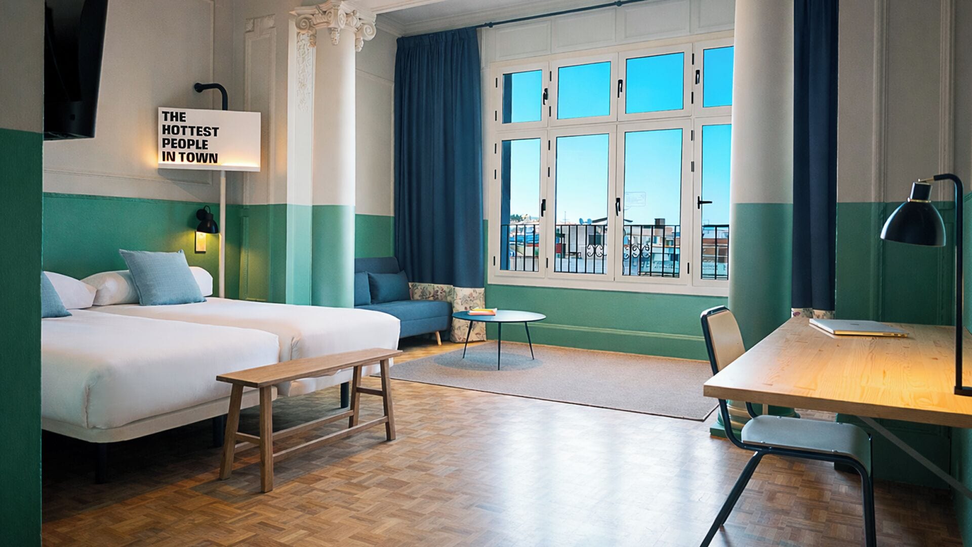 A hotel room with two beds, a desk, a chair, a small table, and a window with curtains.