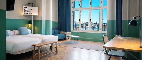 A hotel room with two beds, a desk, a chair, a small table, and a window with curtains.