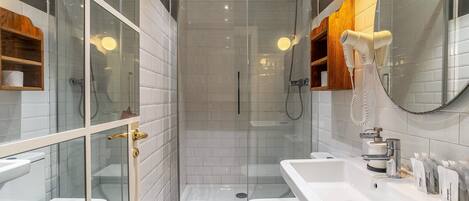 A modern bathroom with a glass-enclosed shower, white tiled walls, a white sink, and a wooden shelf.