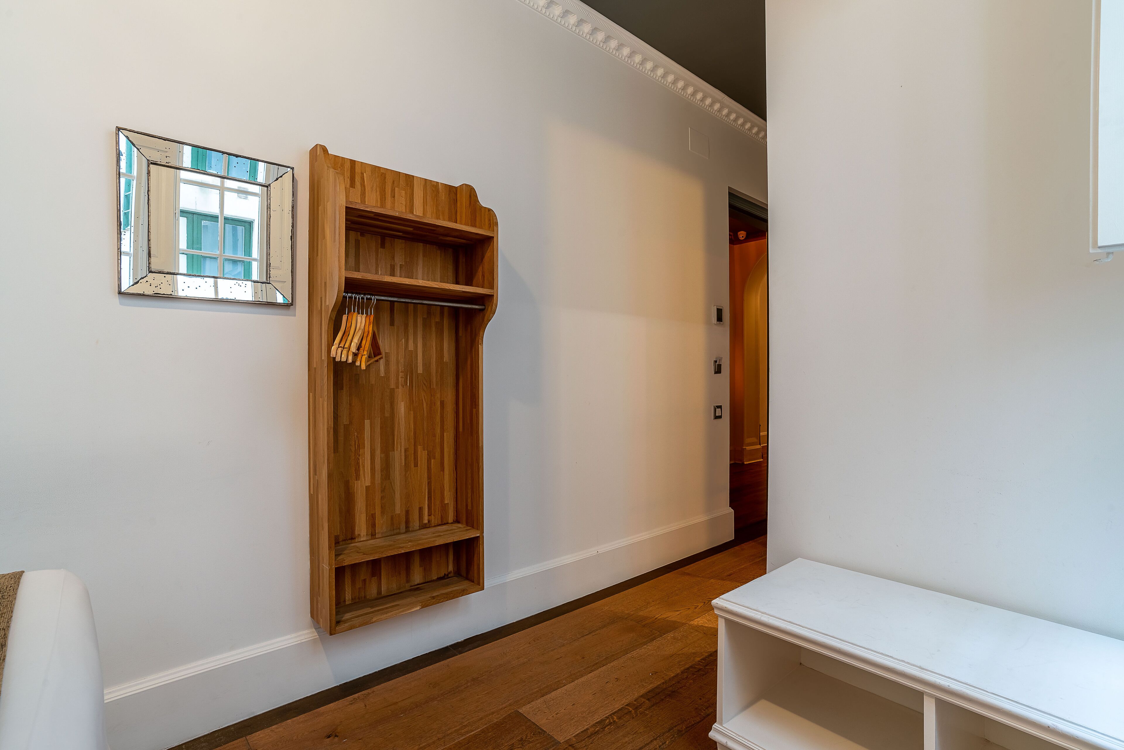 A hallway with a wooden wardrobe, a white bench, and a mirror on the wall.