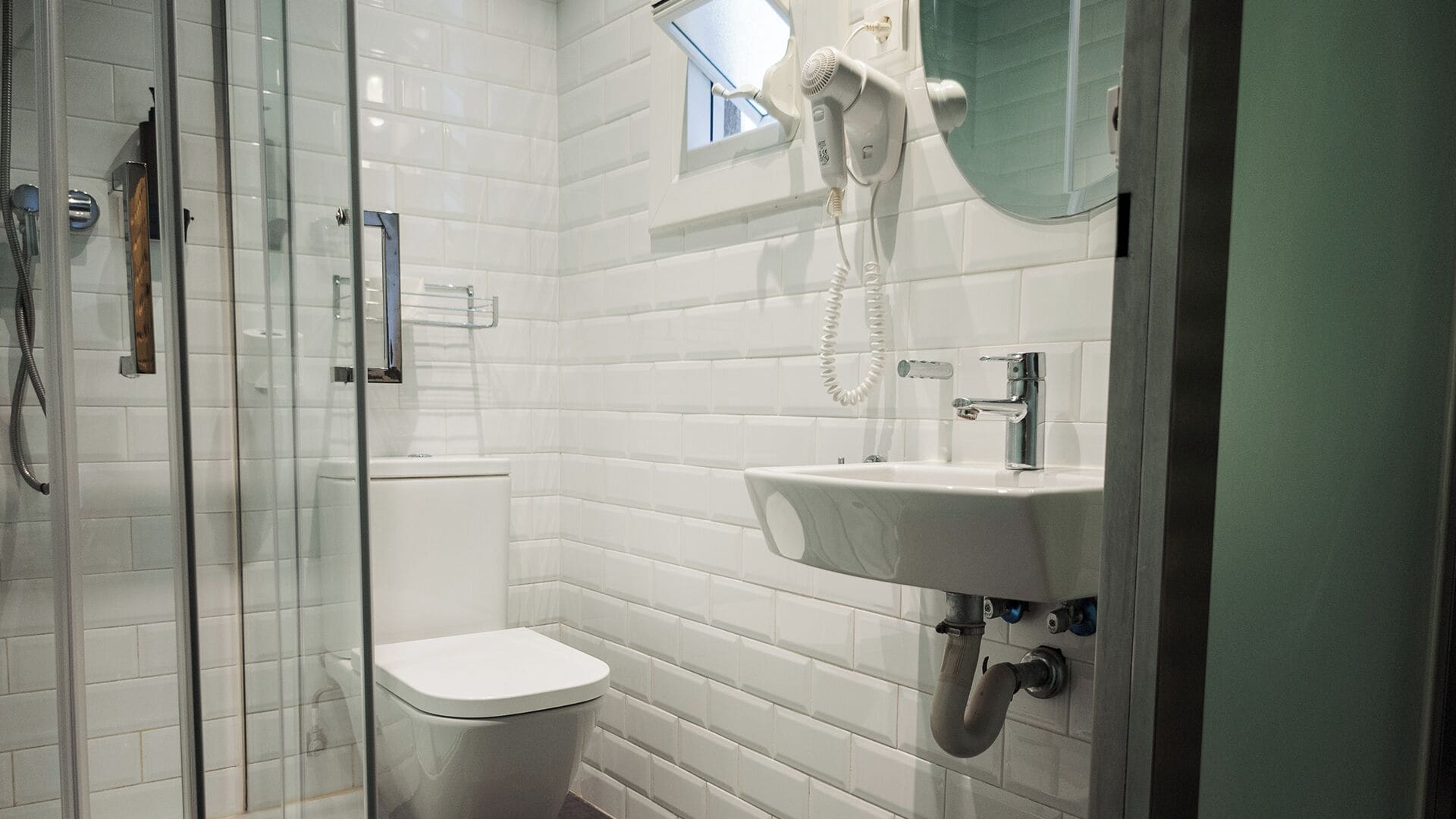 Un baño moderno con cabina de ducha de vidrio, inodoro, lavamanos con espejo y secador de pelo montado en la pared.