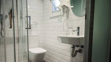 Un baño moderno con cabina de ducha de vidrio, inodoro, lavamanos con espejo y secador de pelo montado en la pared.