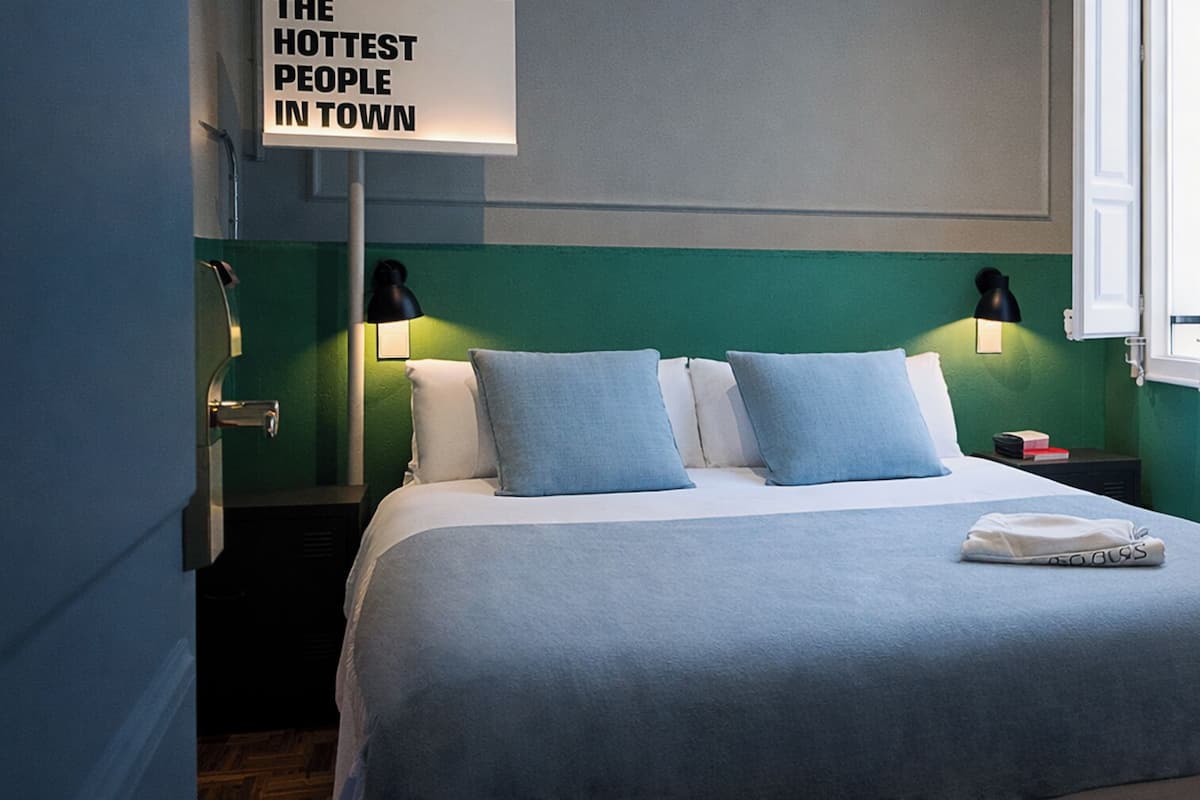 Une chambre d’hôtel avec un lit, deux tables de chevet, une petite table, une lampe et un panneau accroché au mur.