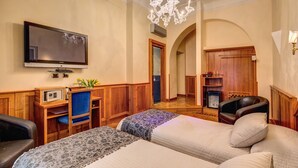 A hotel room with two beds, a television, a desk with a chair, a chandelier, and a wooden wardrobe. - Relais Conte di Cavour de Luxe (Rome)