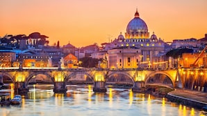 A historic bridge with multiple arches spanning a river, leading to a grand building with a large dome. - Relais Conte di Cavour de Luxe (Rome)