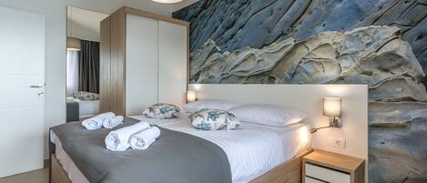 A modern bedroom with a large bed, a nightstand, and a wall mural.