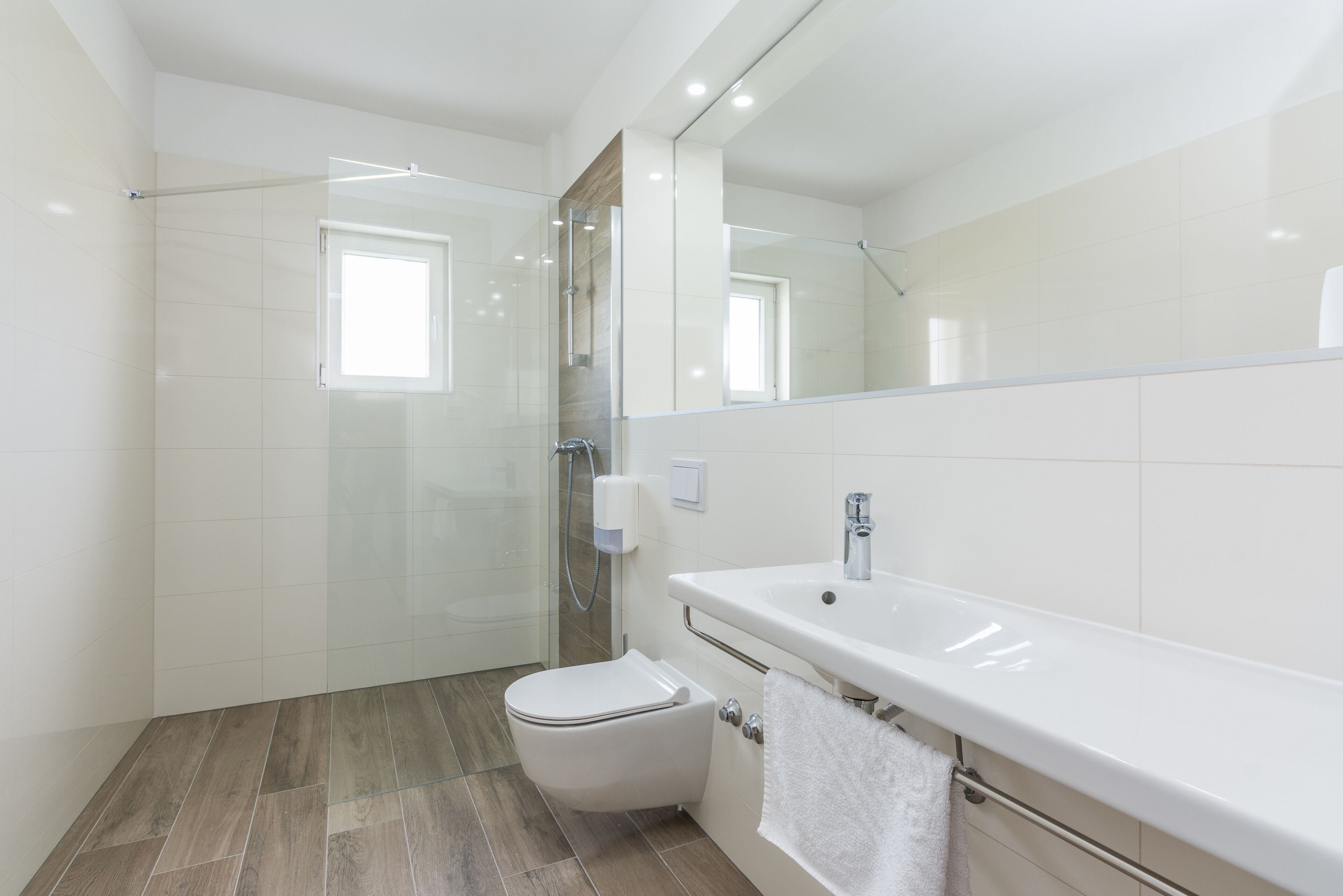 A modern bathroom with a glass-enclosed shower, a white toilet, and a large white sink with a towel rack.