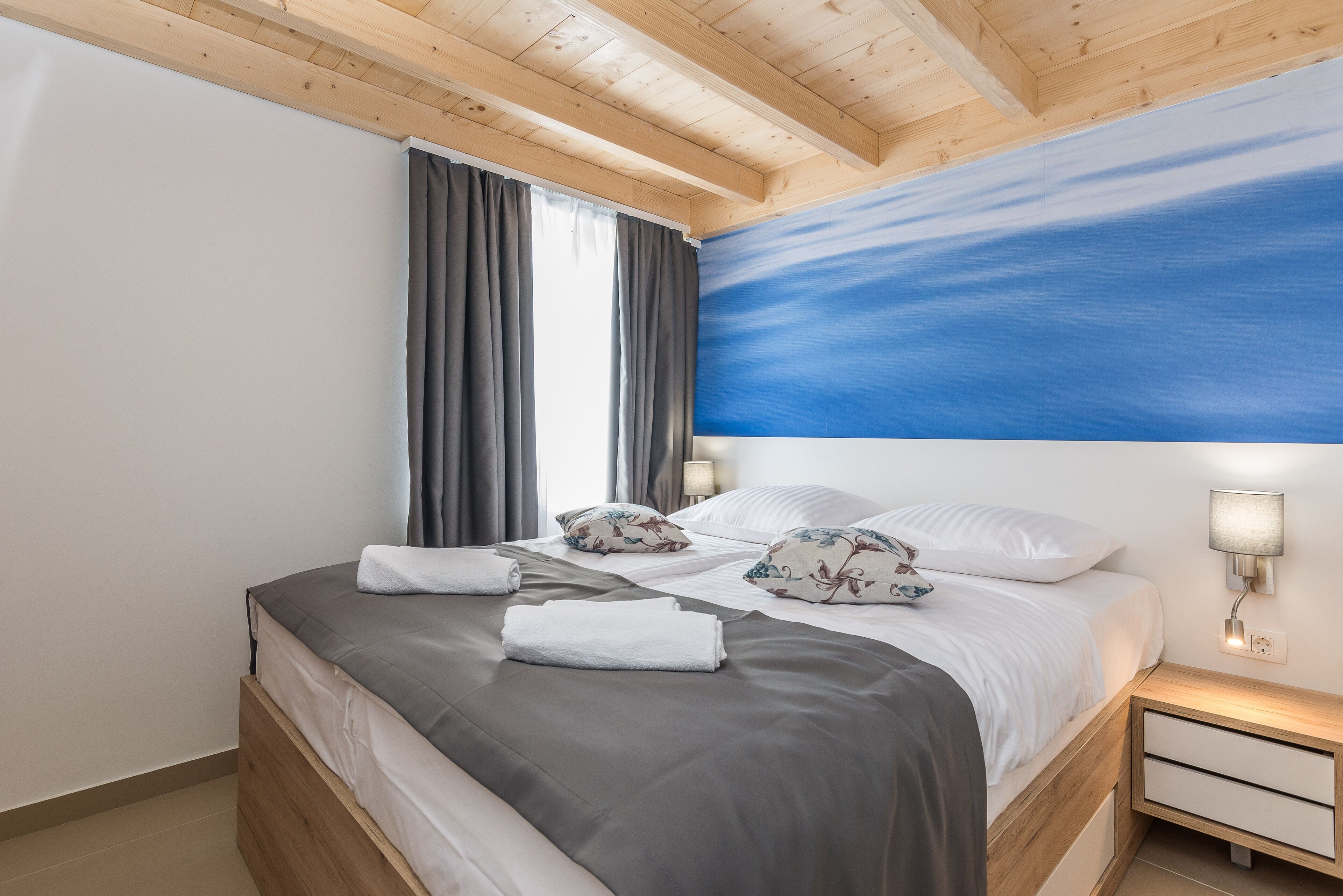 A bedroom with a bed, curtains, a nightstand, and a wall painting.