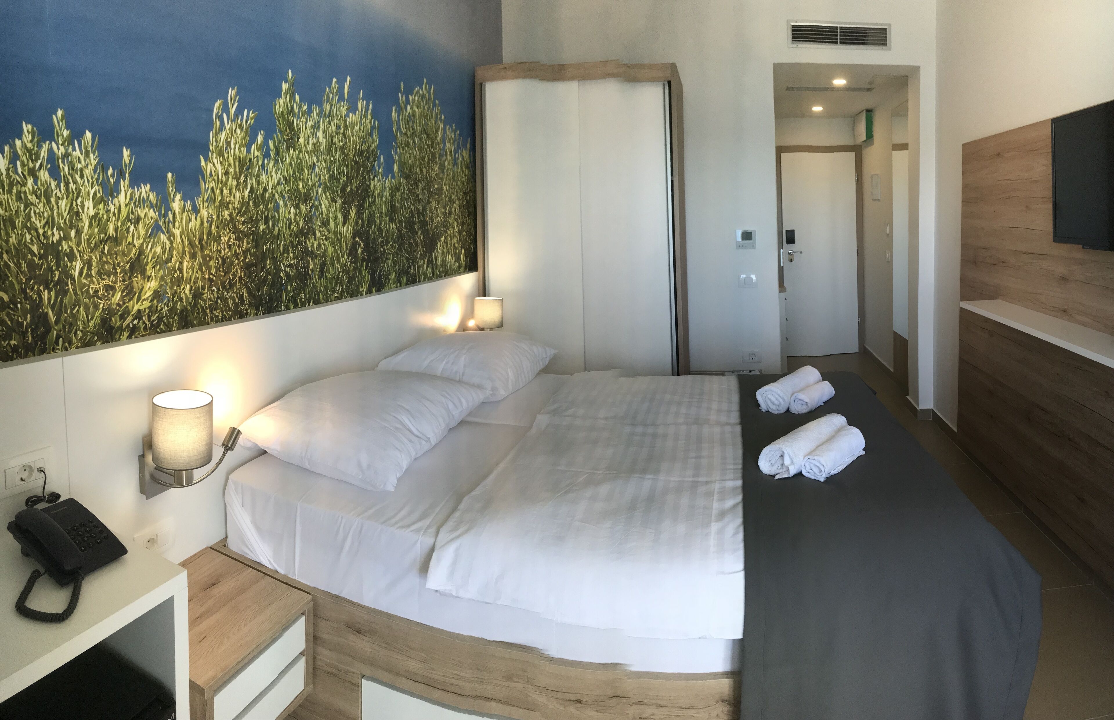 A hotel room with a bed, a bedside lamp, a telephone, and a wall-mounted TV.