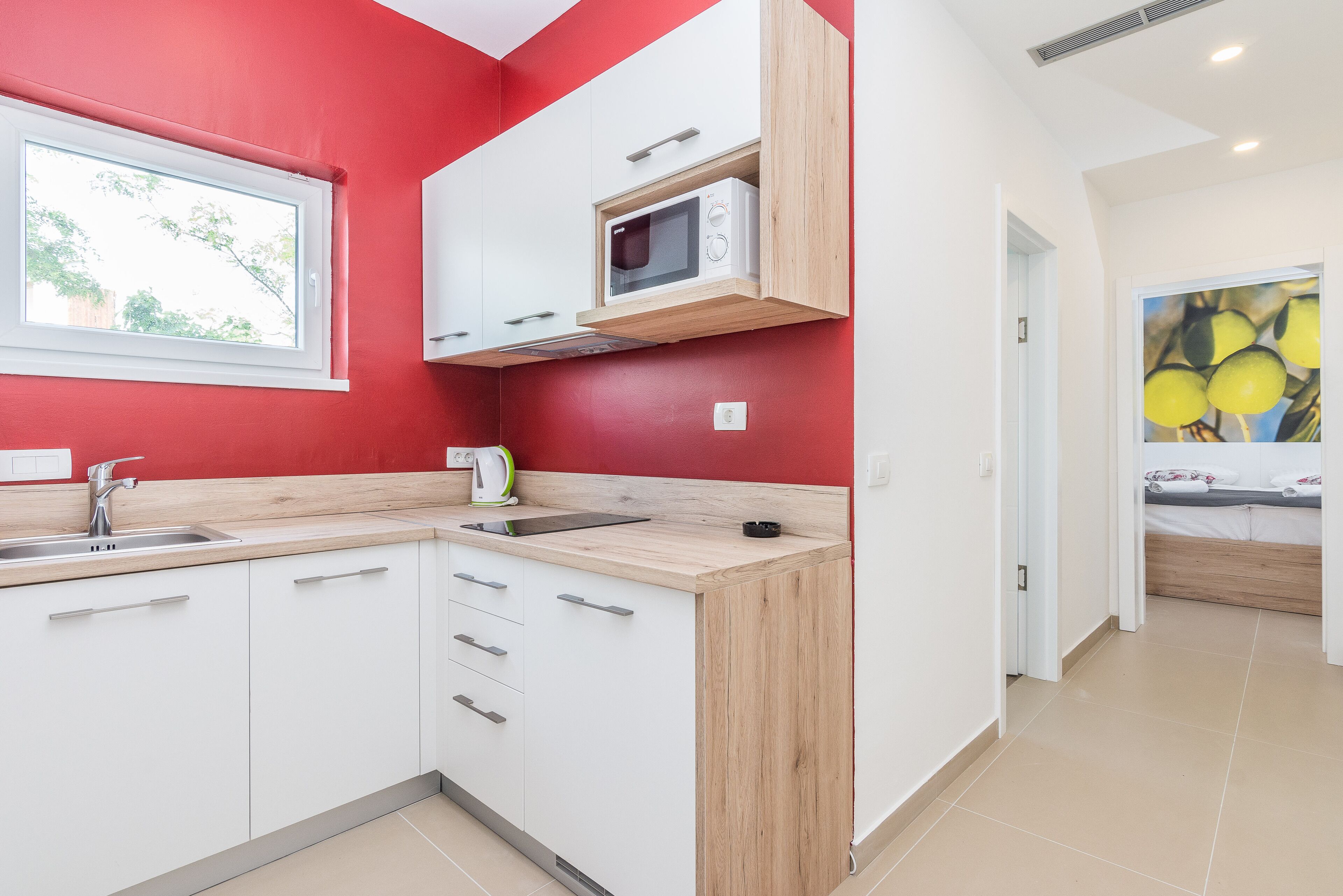A modern kitchen with white cabinets, a wooden countertop, a microwave, and a window.
