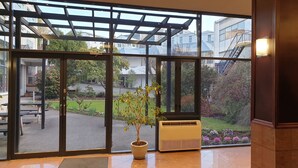 Vista a través de amplios ventanales de un edificio, con una planta en maceta y un equipo de aire acondicionado en el suelo.