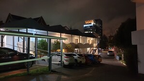 Un estacionamiento con varios coches, un pasillo cubierto y un edificio con un letrero que dice "Hotel".