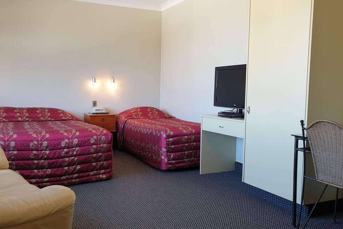 A hotel room with two beds, a desk with a TV, a chair, and a small table with a lamp.