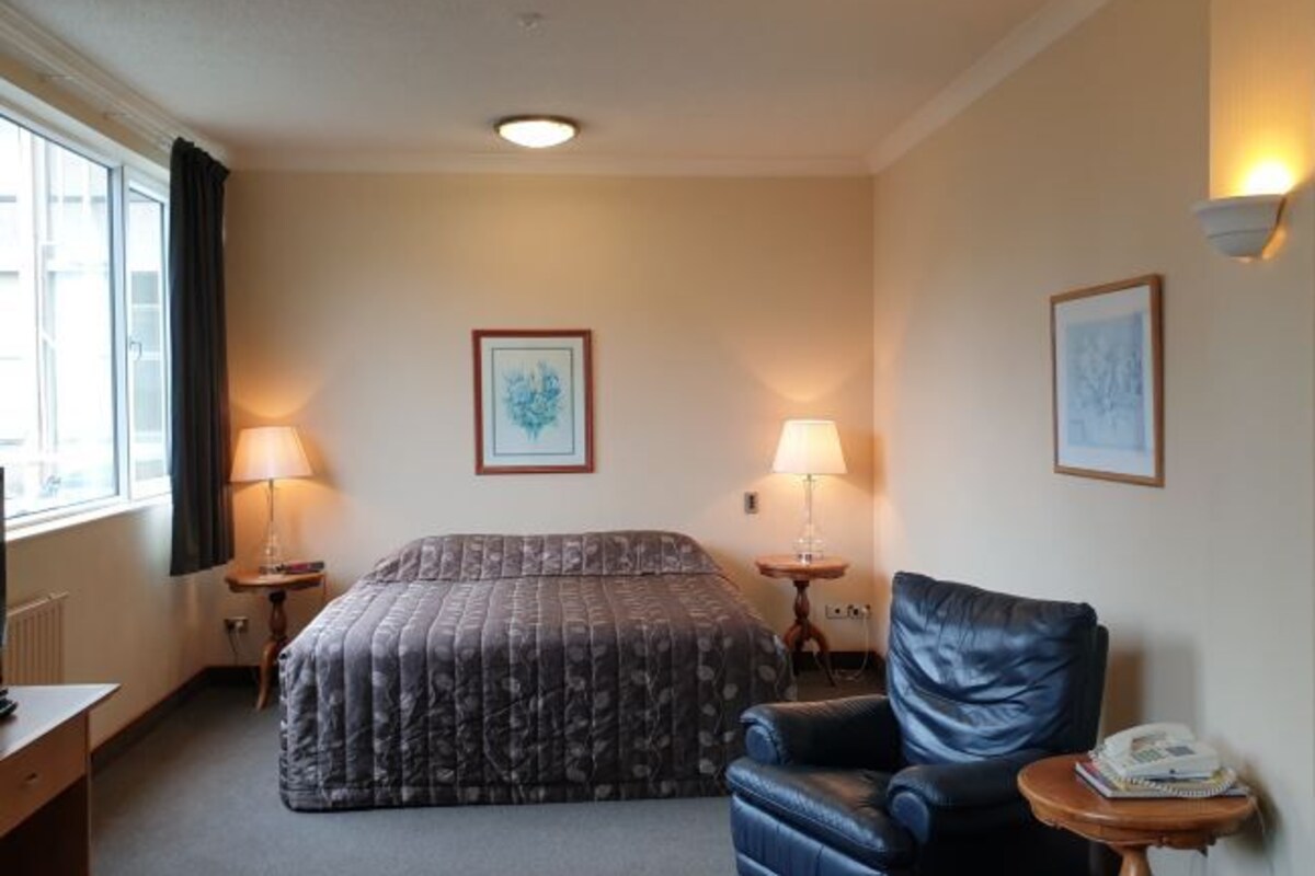 A hotel room with a bed, a leather chair, two bedside lamps, and framed artwork on the walls.