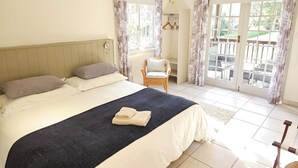A bedroom with a bed, a ceiling fan, a wicker chair, and a view through the glass door.