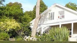 A white house with a porch, surrounded by greenery and trees.