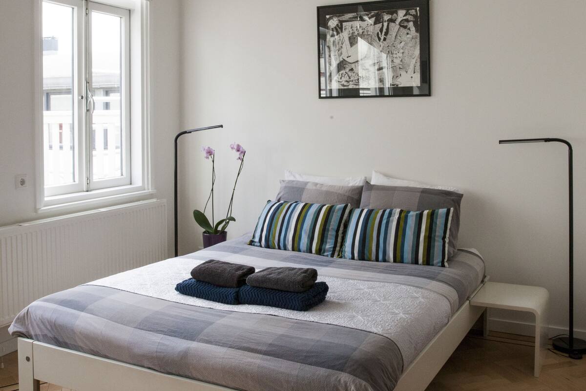 Un dormitorio con una cama, una ventana, una lámpara de pie y un cuadro colgado en la pared.