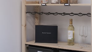 Una habitación con un estante de madera que contiene botes de aperitivos, una botella de vino y vasos. Hay una caja negra con la etiqueta 'GUESTBOOK' y una etiqueta que dice 'PRIVADO' en un cajón.