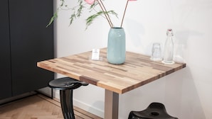 Una mesa de madera con un jarrón de flores rosadas, dos taburetes y un armario negro.