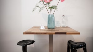 Una mesa con un jarrón de flores rosas, una botella de vidrio y una pequeña señal blanca.