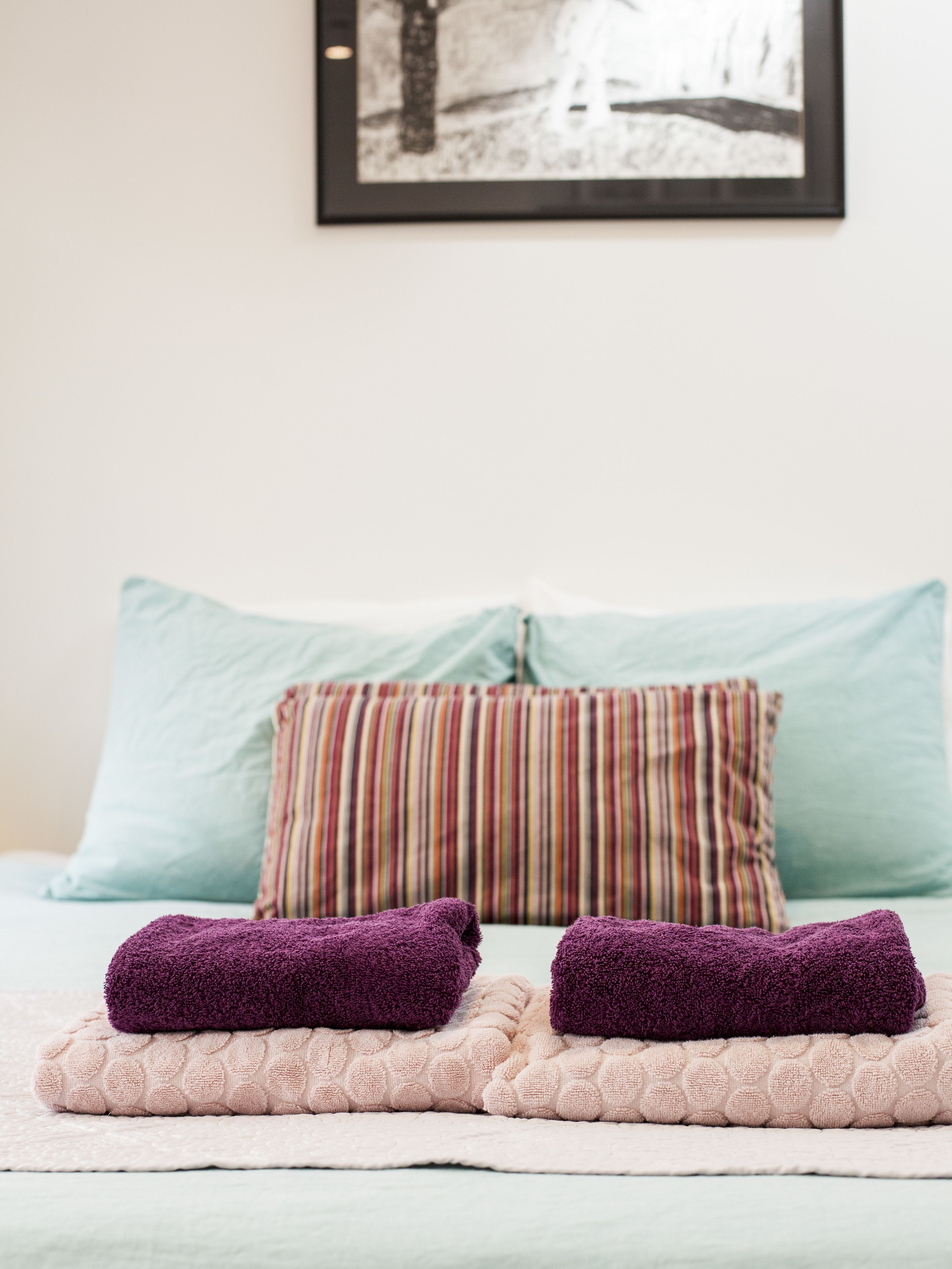A bed with two purple towels, a striped pillow, and a light blue pillow.
