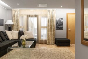 A modern living room with a sofa, ottoman, glass coffee table, and a vase of flowers.