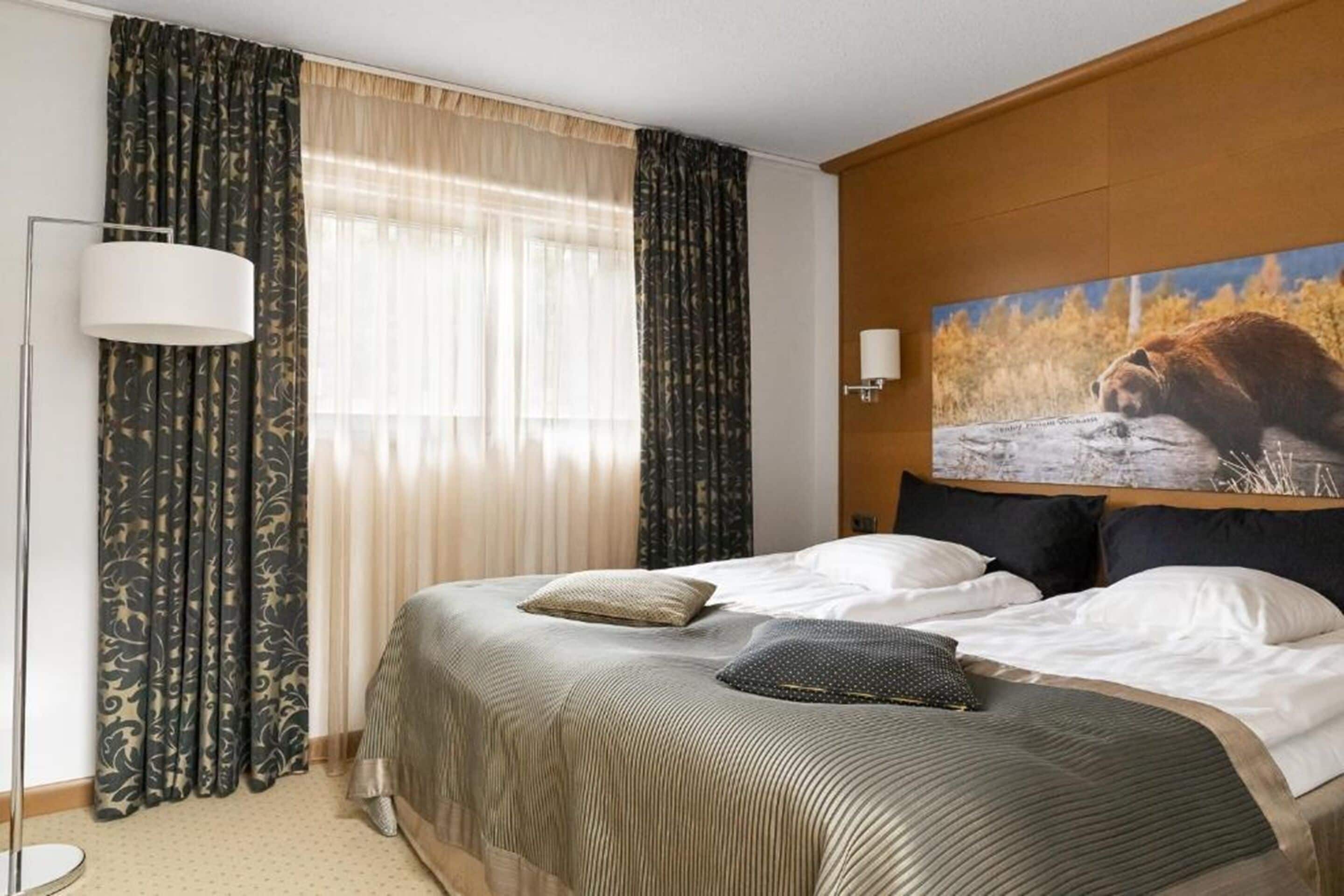 A hotel room with a large bed, two pillows, a lamp, and a painting of a bear on the wall.