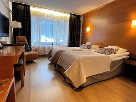 Habitación de hotel con dos camas, un escritorio, una silla, un televisor y una ventana con cortinas.