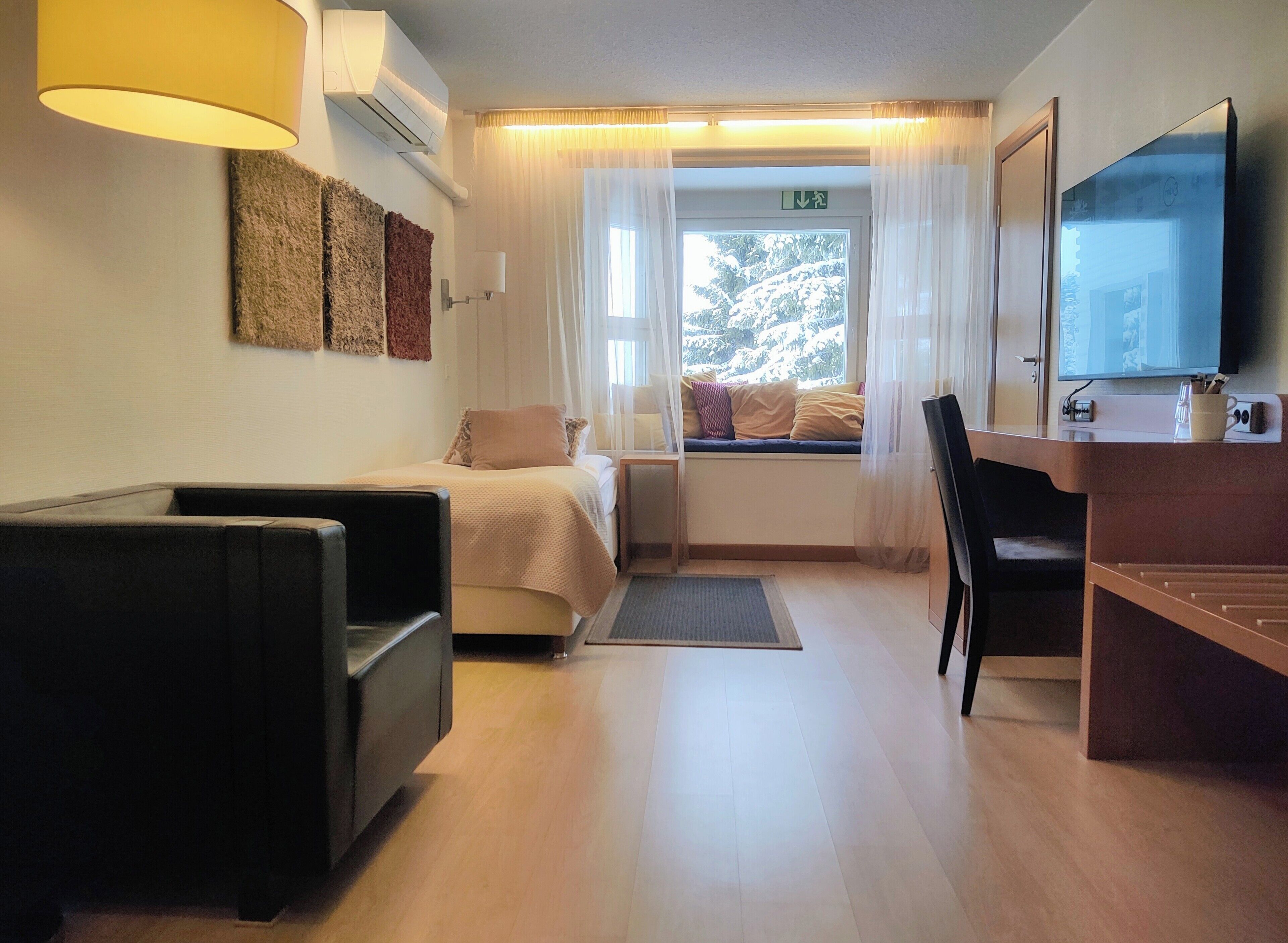 Habitación de hotel con cama, escritorio con silla, televisión y ventana con cortinas.