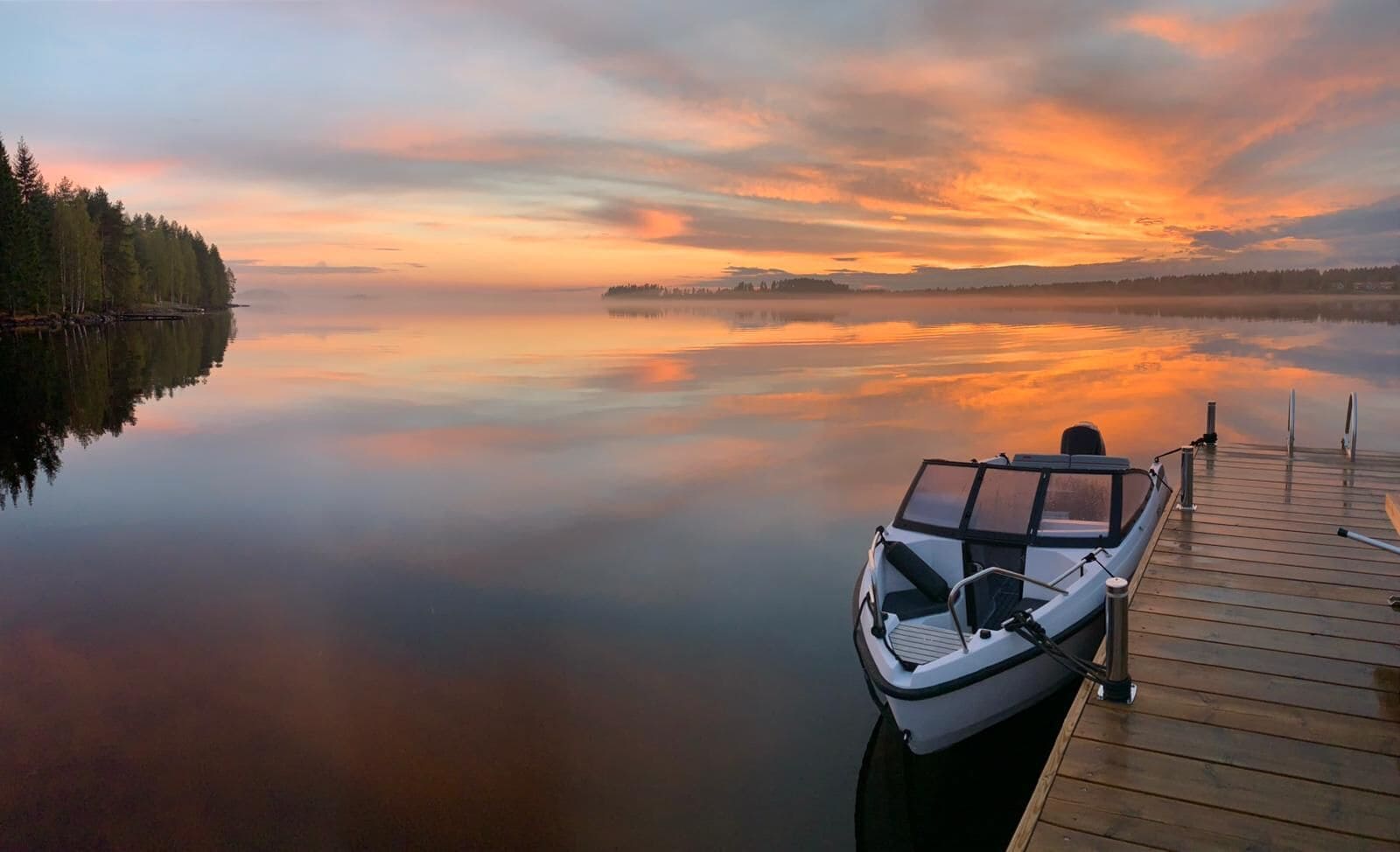 A calm lake with a wooden dock and a small boat.