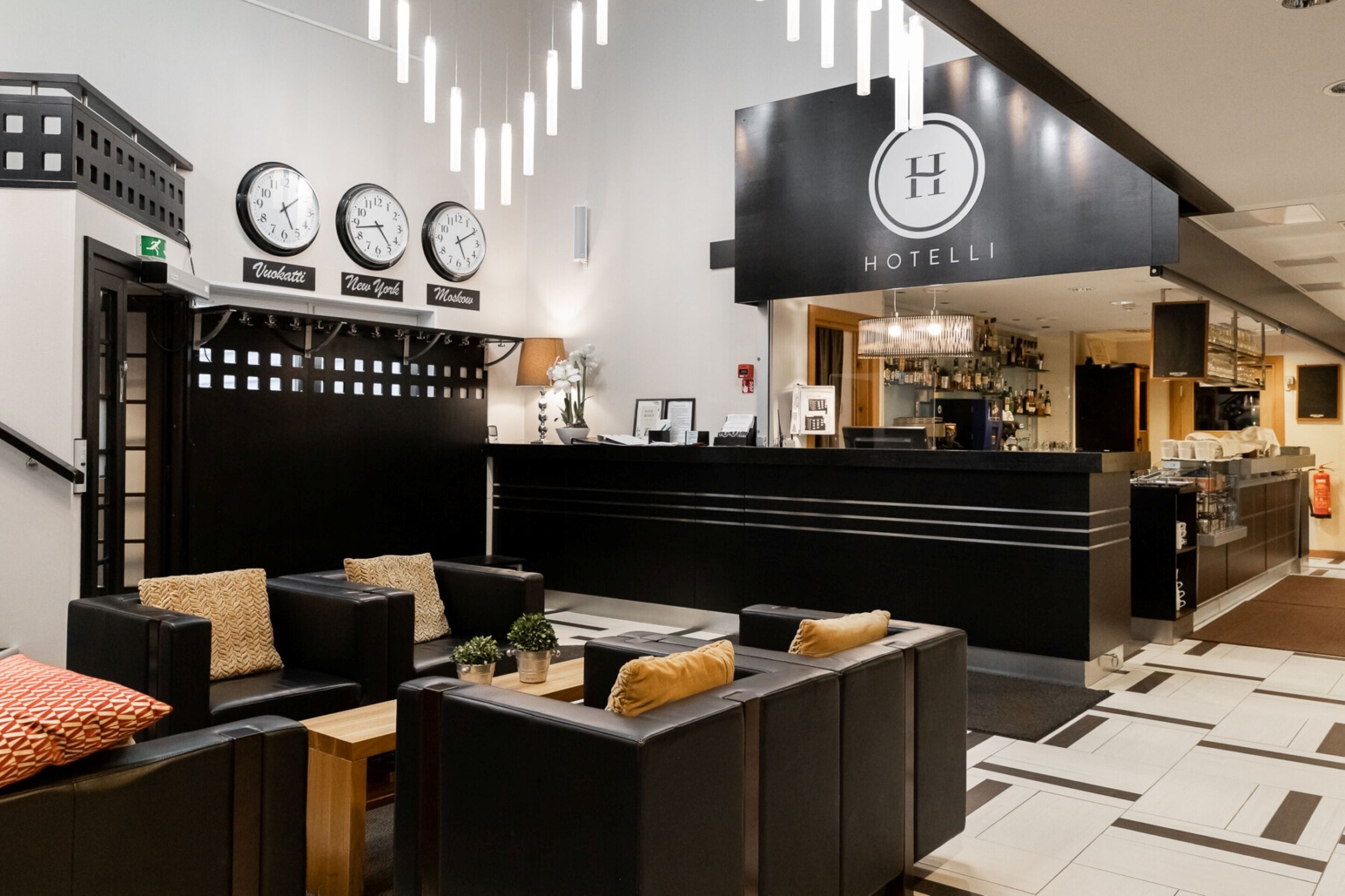 A hotel lobby with a reception desk, seating area, clocks, and a bar.. Hotel Aateli Lakeside