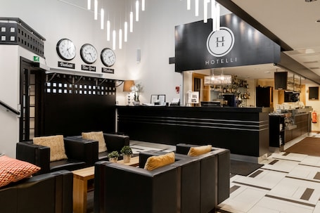 A hotel lobby with a reception desk, seating area, clocks, and a bar.. Hotel Aateli Lakeside