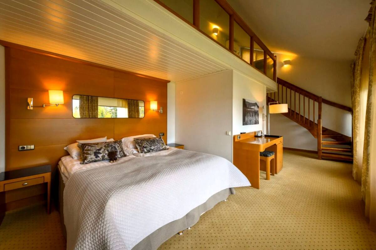 Ein Schlafzimmer mit einem großen Bett, einem Schreibtisch, einem Stuhl, einem Spiegel und einer Treppe.