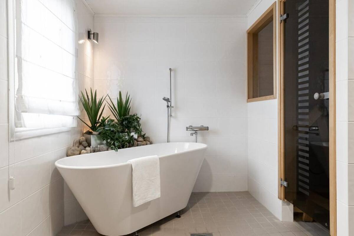 Ein modernes Badezimmer mit freistehender Badewanne, einer Dusche und einem Fenster mit Pflanzen.
