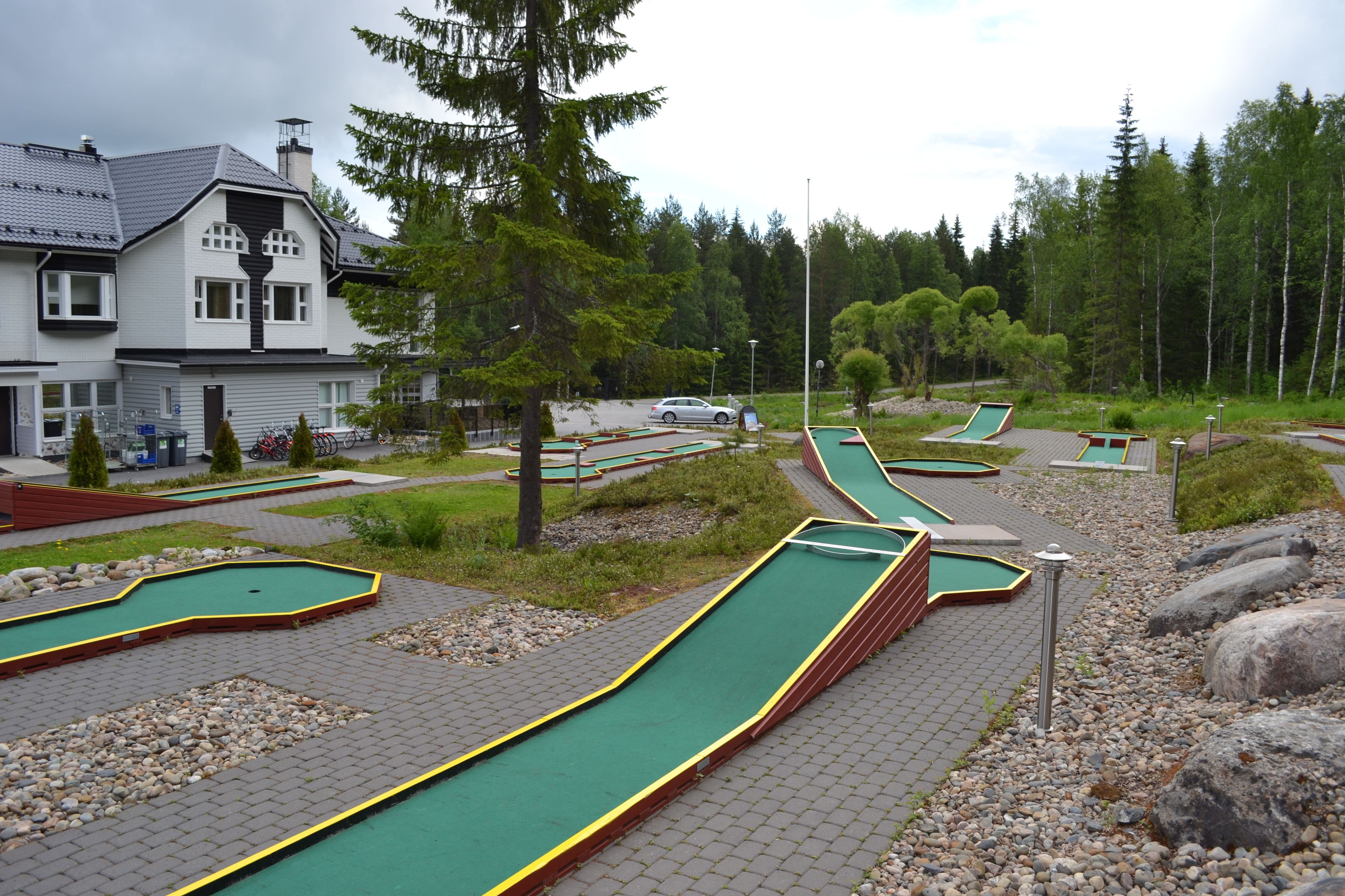 Un camp de mini golf amb diverses pistes, una casa i vegetació al voltant.