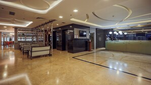 Eine geräumige Lobby mit Marmorboden, einer Rezeption, einer Sitzecke mit Sofas und einem an der Wand montierten Fernseher.